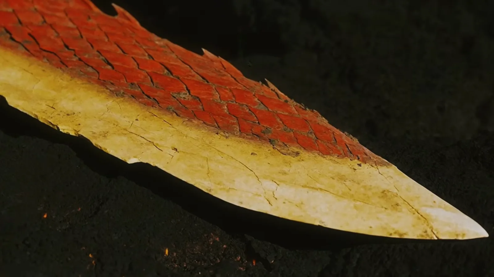 A swordtail dragon’s tail ends in a massive flat blade with red scales along its spine and a pale yellow edge